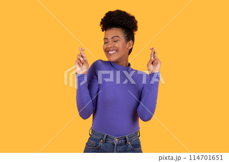 Hispanic woman wearing a purple shirt is gesturing with her hand in a clear and deliberate manner, cross fingers. Her expression is focused, indicating intent behind the gesture she is making. 114701651