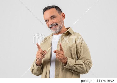 A senior man wearing a tan shirt is smiling and giving a thumbs up gesture. He appears to be expressing approval or agreement with a positive attitude. 114701652