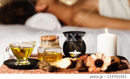 A close-up of spa accessories, including oil bottles, a candle and botanical decorations with a blurry background of spa therapy A close-up of spa accessories, including oil bottles, a candle and botanical decorations with a blurry background of spa therapy 114701841