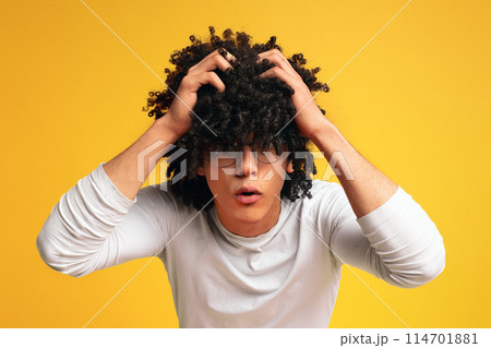 Troubles concept. Shocked emotional african man with bushy hairstyle rending his hair in desperate gesture, orange studio background 114701881