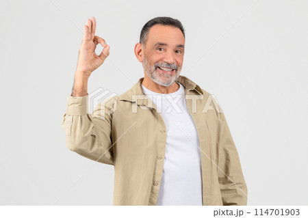 A senior man wearing a white shirt and tan jacket is seen making the Okay sign with his hand. His fingers are split in the iconic OK shape A senior man wearing a white shirt and tan jacket is seen making the Okay sign with his hand. His fingers are split in the iconic OK shape 114701903
