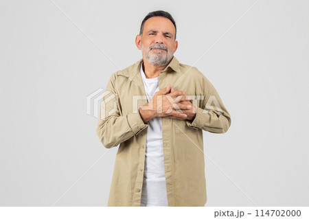 A senior man is standing upright with his hands neatly folded in front of his chest, experiencing heart attack on white background A senior man is standing upright with his hands neatly folded in front of his chest, experiencing heart attack on white background 114702000