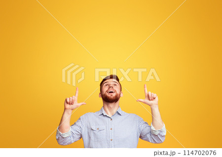 A man standing with hands in the air in front of a bright yellow background. 114702076
