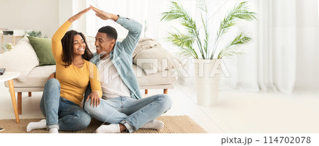 African American couple creating a house shape with hands, emphasizing togetherness, with ample copy space and web-banner layout 114702078