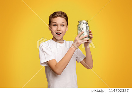 Early financial education. Emotional boy holding glass money box on orange background, copy space 114702327