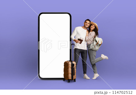 Affectionate couple leaning on each other by a huge smartphone with blank screen, showing off digital technology for travel 114702512