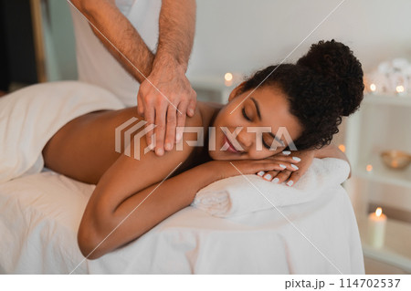 An intimate view of a black lady receiving a relaxing back massage in a cozy spa, with a focus on the hands and comfort 114702537