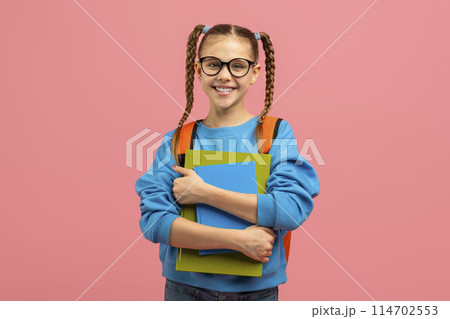This image portrays a content schoolgirl with a friendly demeanor holding notebooks on a pink backdrop 114702553