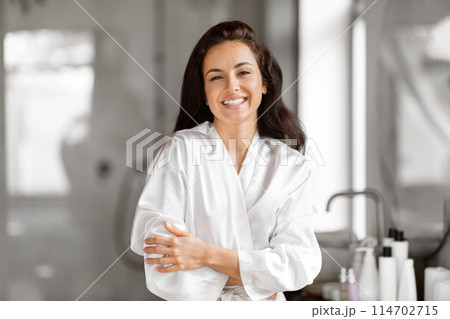 A relaxed woman is pictured in a bathroom, wrapped in a white robe, evoking millennial self-care and skin care moments 114702715