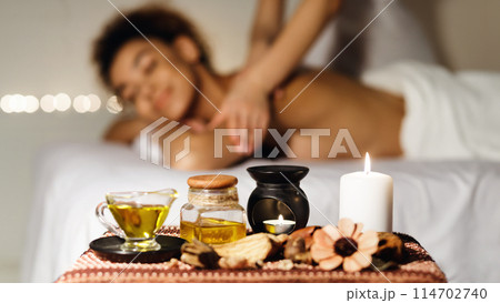 In-focus spa oil and blurred background of an african american woman receiving a massage at a spa with a happy expression 114702740