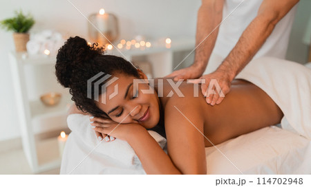 A close-up image of a black lady enjoying a soothing shoulder massage at a spa, with focus on the hands of the therapist and a relaxing atmosphere A close-up image of a black lady enjoying a soothing shoulder massage at a spa, with focus on the hands of the therapist and a relaxing atmosphere 114702948