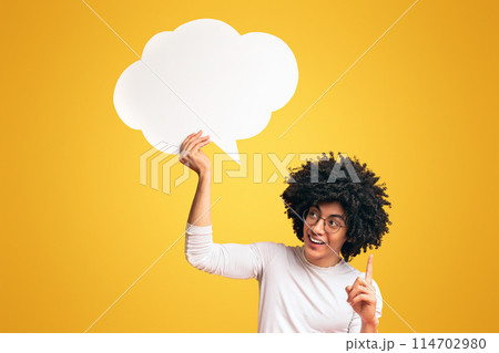 Creative idea. Inspired black man holding an empty speech bubble above his head, orange studio background, empty space 114702980