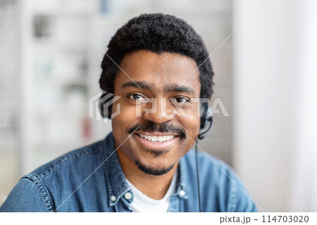 African american guy at home gives a warm and friendly smile to the camera, wearing a headset during a break, closeup African american guy at home gives a warm and friendly smile to the camera, wearing a headset during a break, closeup 114703020
