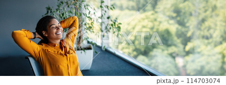 Taking break. Relaxed african american businesswoman resting on chair, leaning back at workplace in office. Happy woman with closed eyes holding hands behind head, panorama with copy space Taking break. Relaxed african american businesswoman resting on chair, leaning back at workplace in office. Happy woman with closed eyes holding hands behind head, panorama with copy space 114703074
