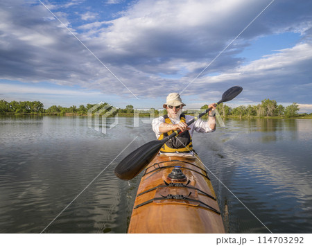 bow view of a senior male paddling a home built wooden sea kayak on a lake in Colorado 114703292
