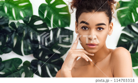 A thoughtful african american woman appears against a backdrop of green foliage, symbolizing a connection with nature and themes related to spa and wellbeing A thoughtful african american woman appears against a backdrop of green foliage, symbolizing a connection with nature and themes related to spa and wellbeing 114703318