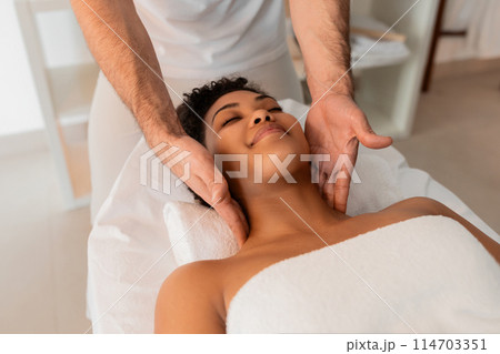 Professional hands focus on massaging the neck of a black lady, emphasizing the importance of self-care at a spa 114703351