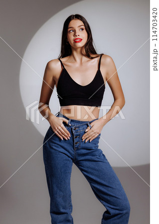 A woman in a black tank top and blue jeans poses for a photo 114703420