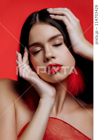 Brunette woman and red feather earrings on a red background. 114703426