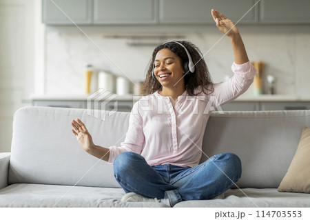 An african american lady is captured in a moment of joy while listening to music with headphones in her home 114703553