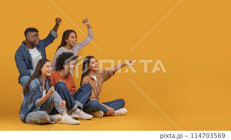 Multiethnic friends excitedly cheering and pointing to the side, exemplifying celebration and happiness in a diverse group, isolated on a yellow background, copy space Multiethnic friends excitedly cheering and pointing to the side, exemplifying celebration and happiness in a diverse group, isolated on a yellow background, copy space 114703569