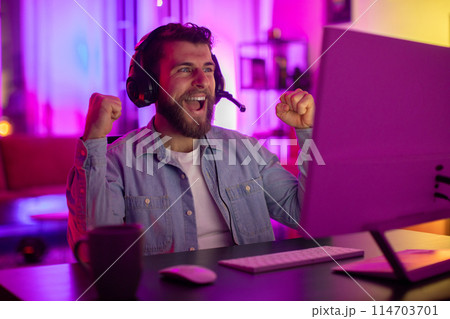 A millennial guy shows an outburst of happiness, clutching his gaming headset, portraying the joy and addiction of home gaming A millennial guy shows an outburst of happiness, clutching his gaming headset, portraying the joy and addiction of home gaming 114703701
