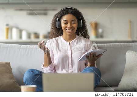 African American woman smiles engagingly while video conferencing from home, her headphones suggest an immersive call 114703722