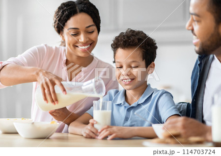 An african american mother pours milk into her son's glass as the family enjoys a morning routine together in their kitchen, embracing family and health 114703724