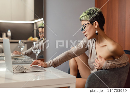 A sexy girl with short hair and glasses is sitting indoors at a laptop, chatting and working online 114703989