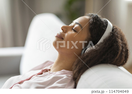 This image captures a moment of tranquility where a black millennial lady rests peacefully on a comfortable white couch at her home, showcasing everyday life This image captures a moment of tranquility where a black millennial lady rests peacefully on a comfortable white couch at her home, showcasing everyday life 114704049