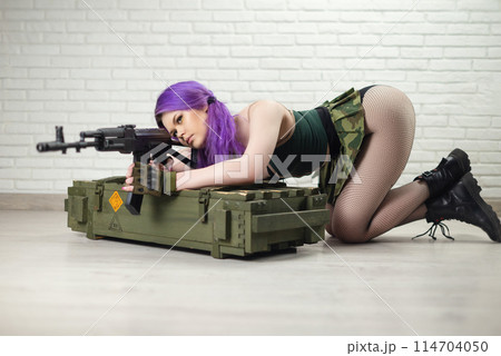 hot girl in a short sexy military skirt with a Kalashnikov assault rifle and a gun case on a brick wall background copy paste 114704050