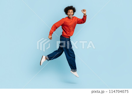A high-spirited young african american man with bushy hair appears to be running joyously, depicting freedom and happiness, against a blue isolated background A high-spirited young african american man with bushy hair appears to be running joyously, depicting freedom and happiness, against a blue isolated background 114704075