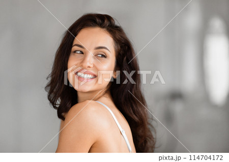 Cheerful lady glances back with a radiant smile, embodying optimism in a grayscale bathroom scene, copy space 114704172