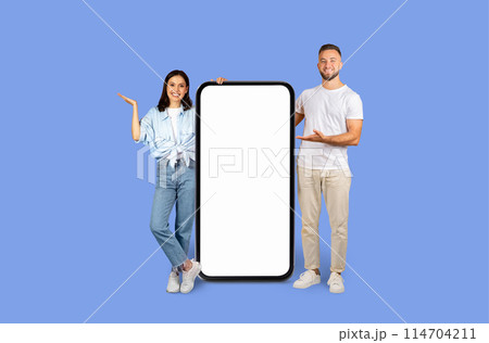 A man and a woman standing, cheerfully presenting a blank large smartphone model to be used for advertising purposes A man and a woman standing, cheerfully presenting a blank large smartphone model to be used for advertising purposes 114704211
