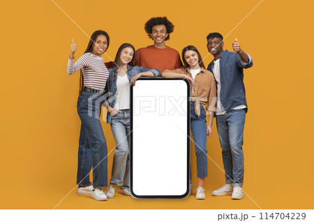 An international team of friends surrounds a large blank smartphone screen, depicting a concept of a connected, multiethnic, and multiracial team isolated on orange An international team of friends surrounds a large blank smartphone screen, depicting a concept of a connected, multiethnic, and multiracial team isolated on orange 114704229