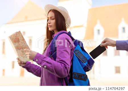 A millennial lady, appearing as a student, is absorbed in reading a map outdoors with European architecture in the background, unaware of being pickpocketed A millennial lady, appearing as a student, is absorbed in reading a map outdoors with European architecture in the background, unaware of being pickpocketed 114704297