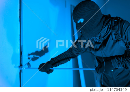 A caught-in-action shot of a thief cautiously opening a glass door while exiting, denoting the silent danger of burglary at an apartment at night 114704349