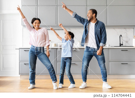 Funny positive African American family dancing in modern grey kitchen, happy black father mother and son enjoying time together at home Funny positive African American family dancing in modern grey kitchen, happy black father mother and son enjoying time together at home 114704441
