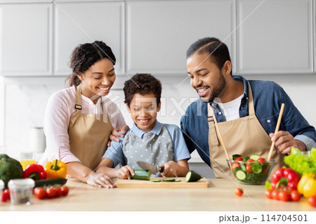 An African American family enjoys quality time preparing a meal together in the kitchen, highlighting family togetherness 114704501