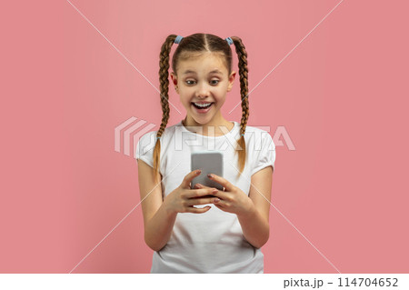 Young caucasian girl expressing amazement at smartphone content, isolated on pink background with a vibrant teen expression Young caucasian girl expressing amazement at smartphone content, isolated on pink background with a vibrant teen expression 114704652