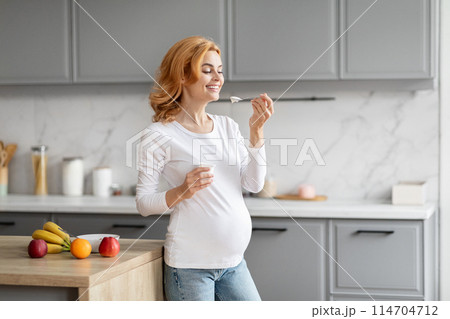 Cheerful european pregnant woman tasting yogurt in a contemporary kitchen, emphasizing healthy nutrition during pregnancy Cheerful european pregnant woman tasting yogurt in a contemporary kitchen, emphasizing healthy nutrition during pregnancy 114704712