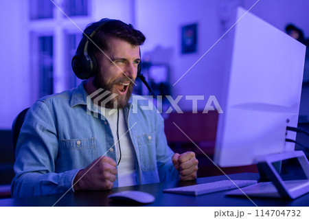 A millennial guy's intense reaction exemplifies the emotional highs and lows of gaming at home, showcasing the potential for addiction within the gamer culture A millennial guy's intense reaction exemplifies the emotional highs and lows of gaming at home, showcasing the potential for addiction within the gamer culture 114704732