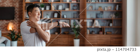 Active asian mature man stretching arm muscles, doing warmup exercises at home, working out in living room interior. Middle aged korean male having domestic training, panorama with copy space Active asian mature man stretching arm muscles, doing warmup exercises at home, working out in living room interior. Middle aged korean male having domestic training, panorama with copy space 114704733