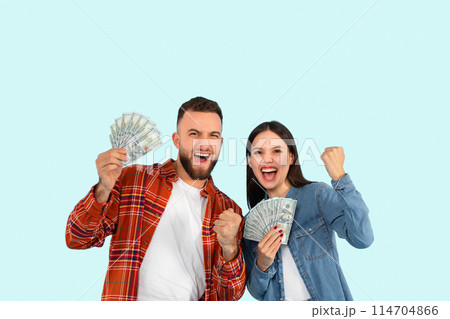 A young man and woman excitedly display their money, celebrating with a joyful expression against a blue background 114704866