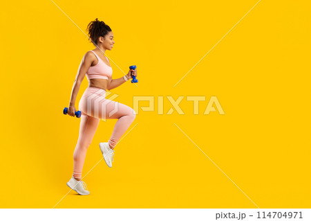 Determined african american lady engaged in a rigorous fitness routine with dumbbells, highlighting strength and focus, against an isolated yellow background Determined african american lady engaged in a rigorous fitness routine with dumbbells, highlighting strength and focus, against an isolated yellow background 114704971