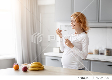 European pregnant lady enjoys a nutritious yogurt in her modern kitchen to support her well-being, copy space European pregnant lady enjoys a nutritious yogurt in her modern kitchen to support her well-being, copy space 114704990