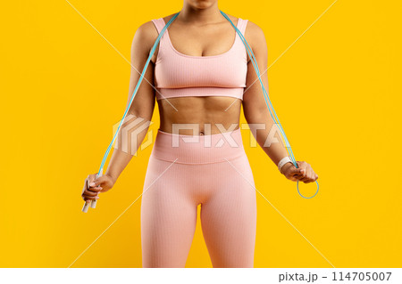 Strong african american fitness lady holding a jump rope, exemplifying health and exercise, preparing for a workout session, isolated on a bright yellow background Strong african american fitness lady holding a jump rope, exemplifying health and exercise, preparing for a workout session, isolated on a bright yellow background 114705007