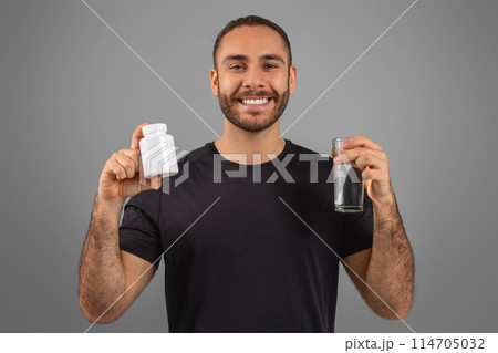 A cheerful man with a bottle of pills and a glass of water, promoting a healthy lifestyle and supplements 114705032