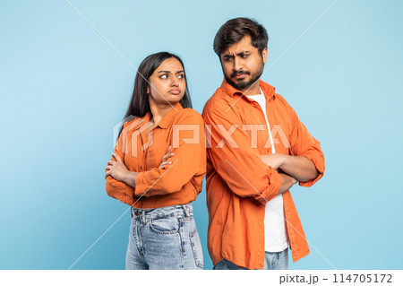 Indian man and woman facing away from each other with crossed arms, signaling a disagreement, against blue background 114705172