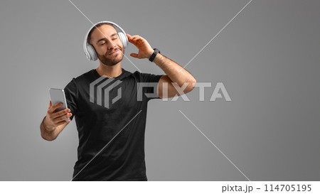 Relaxed man in activewear enjoys music on his smartphone, embodying leisure and enjoyment, using headphones 114705195